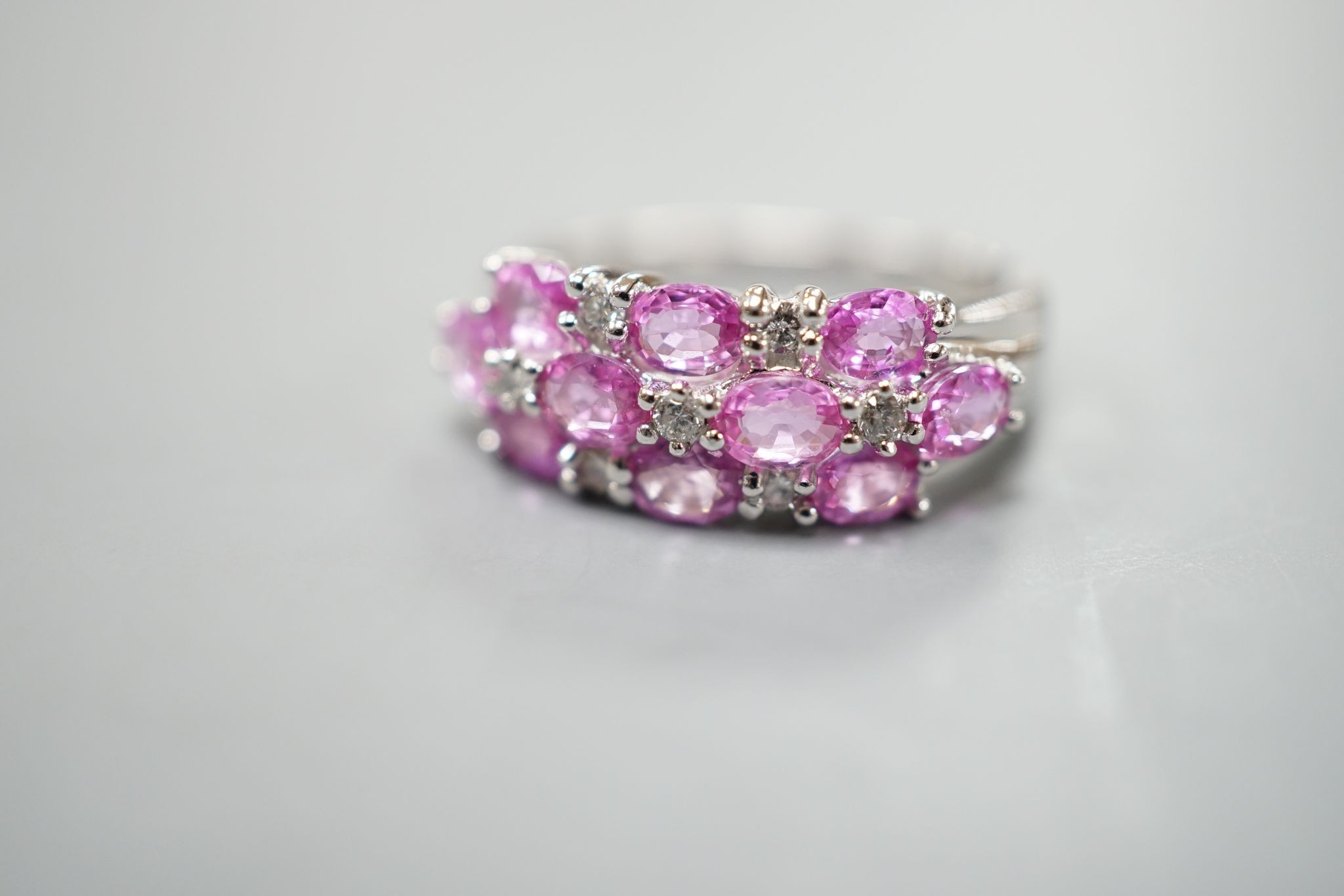 A modern 14k white metal, pink sapphire and diamond cluster set half hoop dress ring, size O, gross weight 4.6 grams.